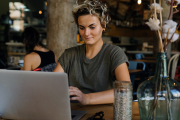 Hipster girl is reading news on a screen of a modern portable computer while sitting in a cafe. Young entrepreneur woman is waiting for the skype call while having breakfast in a modern cafe.