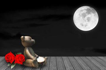 Lonely Old clay cute bear looking to the full moon with two red roses on wooden floor.Image of full moon furnished by NASA.