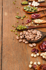 Assortment of beans and lentils in wooden spoon on teak wood background