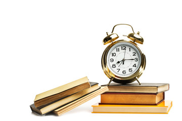 Reloj de metal dorado con libros apilados sobre fondo blanco aislado. Vista de frente. Copy space