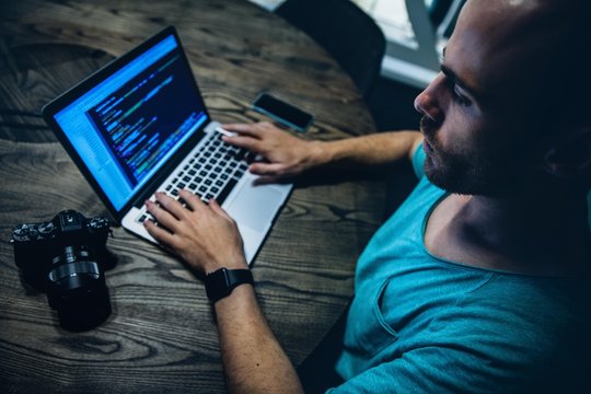 Young male adult working late at night with laptop and camera