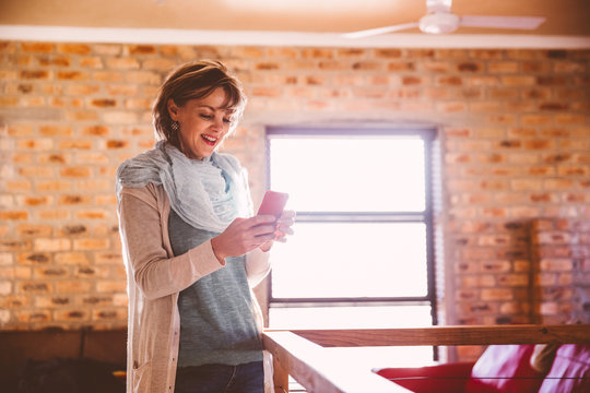 Caucasian woman standing in living room using her mobil phone