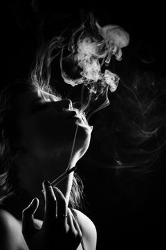 young woman smoking cigarette on black background, monochrome