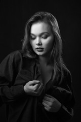 Fototapeta na wymiar beautiful young sensual woman in blouse at black background undressing, monochrome