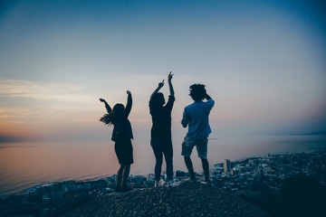 Group of multi-ethnic friends dancing outside on a rock at sunset