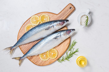 Fish dish cooking with various ingredients. Fresh raw fish decorated with lemon slices and herbs on wooden table.