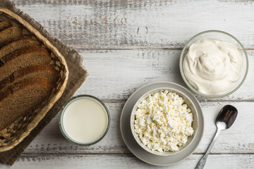 Dairy farm food: curd cheese and cream in bowls, milk and fresh bread in basket on rustic background, top view with copy space