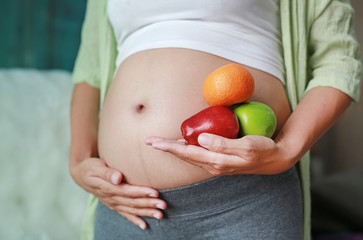 Pregnant woman holding Green-Red Apple and Orange fruit at her belly. Dieting Concept. Healthy Lifestyle.