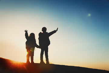 Silhouettes of happy little boy and girl hiking in sunset