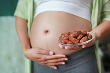 Pregnant woman holding Sweet dried Date Palm fruit at her belly. Dieting Concept.