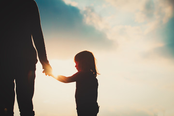 silhouette of little girl holding parent hand at sunset - obrazy, fototapety, plakaty