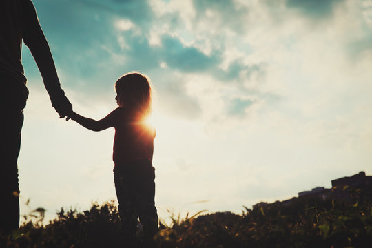 silhouette of little girl holding parent hand at sunset