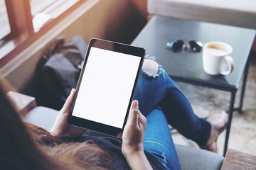 Mockup image of woman's hands holding black tablet pc with white blank screen sitting in modern cafe , coffee cup of hot latte and sunglasses on the table