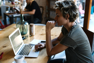Web designer is reading emails on a screen of a modern portable computer while sitting in a cafe. Hipster girl is chatting with friends via social networks on a laptop and a smartphone.