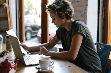Student girl is reading papers while sitting in cafe with a portable computer while preparing to...