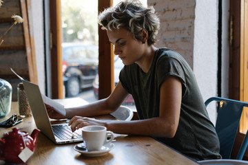 Hipster girl is typing emails by a modern portable computer while sitting in a coffee shop. Young...