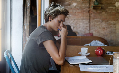 Young business woman has a serious business talk by a mobile phone with partners while sitting in a coffee shop. Young blogger is working in the new post while sitting in a modern coworking space.