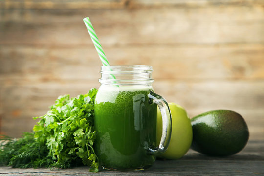 Green smoothie in glass jar with apple, avocado, parsley and dill on wooden table