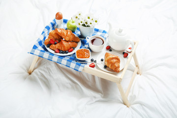 Tasty breakfast in bed on wooden tray
