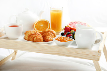 Tasty breakfast in bed on wooden tray