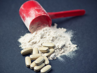 Fitness and sports concept with a spilled scoop of protein powder necessary nutrition for muscle recovery after an intensive workout, next to a bcaa pills