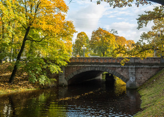 Fototapeta na wymiar Old stone bridge crossing over the city river canal. Yellow foliage in the autumn park. Riga, Latvia.
