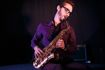 Fototapeta na wymiar Young saxophonist. Pink stage lightening