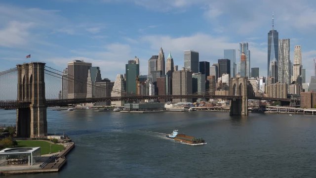 A daytime wide establishing shot of the Manhattan Skyline with a barge traveling under the Brooklyn Bridge.  
