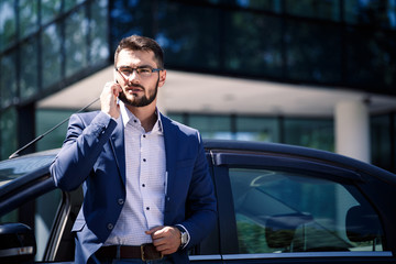 Young businessman standing near the car and holding phone