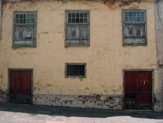 old typical Spanish house in the tenerife with crumbling yellow plaster walls and fading green painted windows on a sloping hilly street