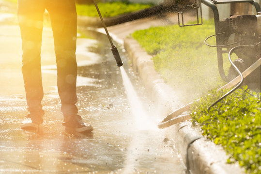 High pressure deep cleaning.Worker cleaning driveway with gasoline high pressure washer with rim light effect,professional cleaning services.