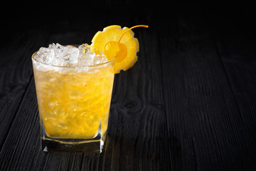 Yellow alcohol cocktail with cherry and lemon on black wooden background