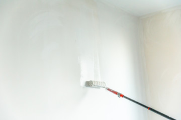Paint stick roller painting a blank wall, in empty white room with copy space.