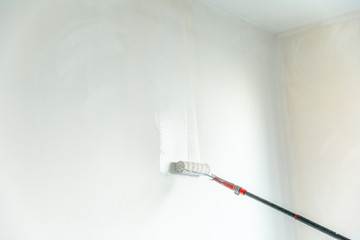 Paint stick roller painting a blank wall, in empty white room with copy space. © bennymarty