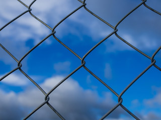 Closeup of metal chainlink fence in front of dramatic blue cloudy sky