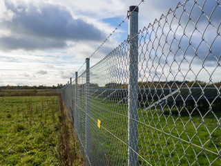 Long metal chainlink fence securing solar or photovoltaic panel farm with dramatic cloudy sky in North Germany