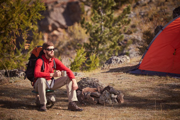 Fototapeta premium Backpacker having rest near orange tent with cup in hand.