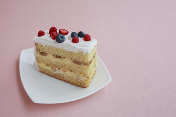 a piece of cake with blueberries and raspberries is on the table with a pink color