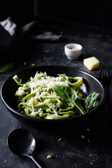 Green spinach pasta with cheese and pine nuts in black bowl. Closeup view, selective focus