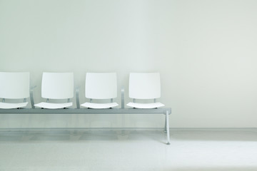 Waiting hall chairs forming a row against a white wall background. Empty copy space for Editor's...