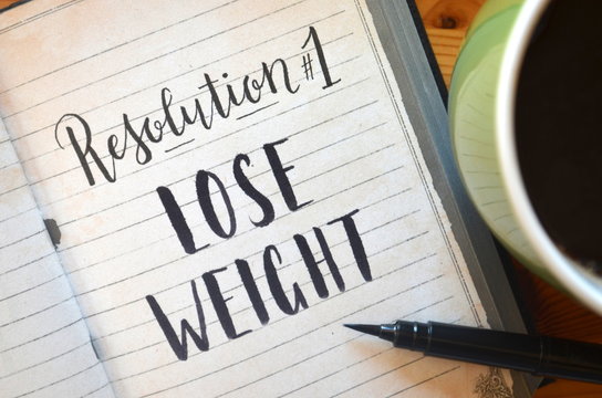 Resolution No. 1 LOSE WEIGHT hand-lettered in notebook with cup of coffee on desk