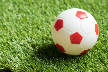 Fototapeta premium Toy red and white color football on artificial green grass background