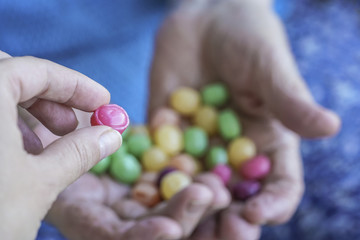 young hand picks a hard candy from palm of an old person