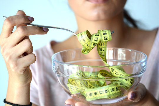 Young Woman On Diet Eating A Yellow Measurement Tape From A Transparent Bowl