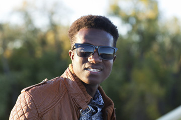 Handsome young black man in sunglasses and a leather jacket on a fall day