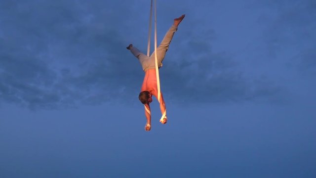 Man is an aerial acrobat on belts, he stands high in the sky.