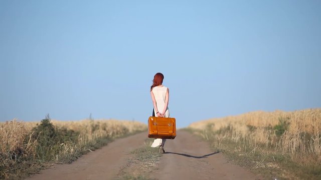 Young redhead girl walking with travel suitcase at countryside road