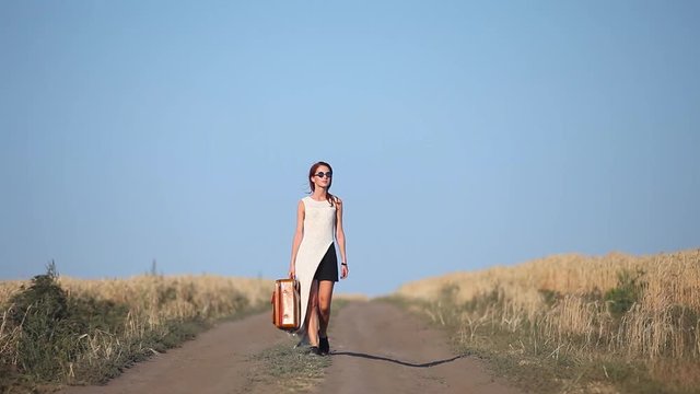 Young redhead girl walking with travel suitcase at countryside road