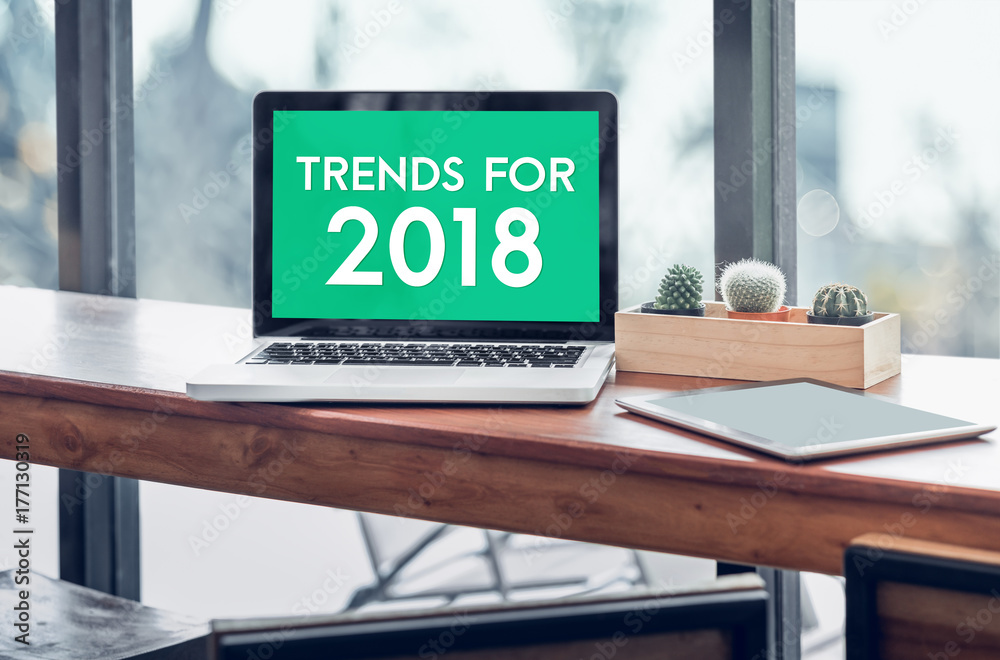 Poster trends for 2018 word in laptop computer screen with tablet on wood stood table in at window with blu