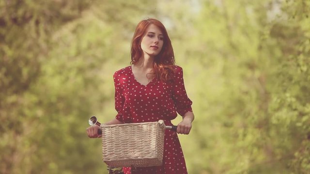 Redhead woman in red dress with bike at outdoor.